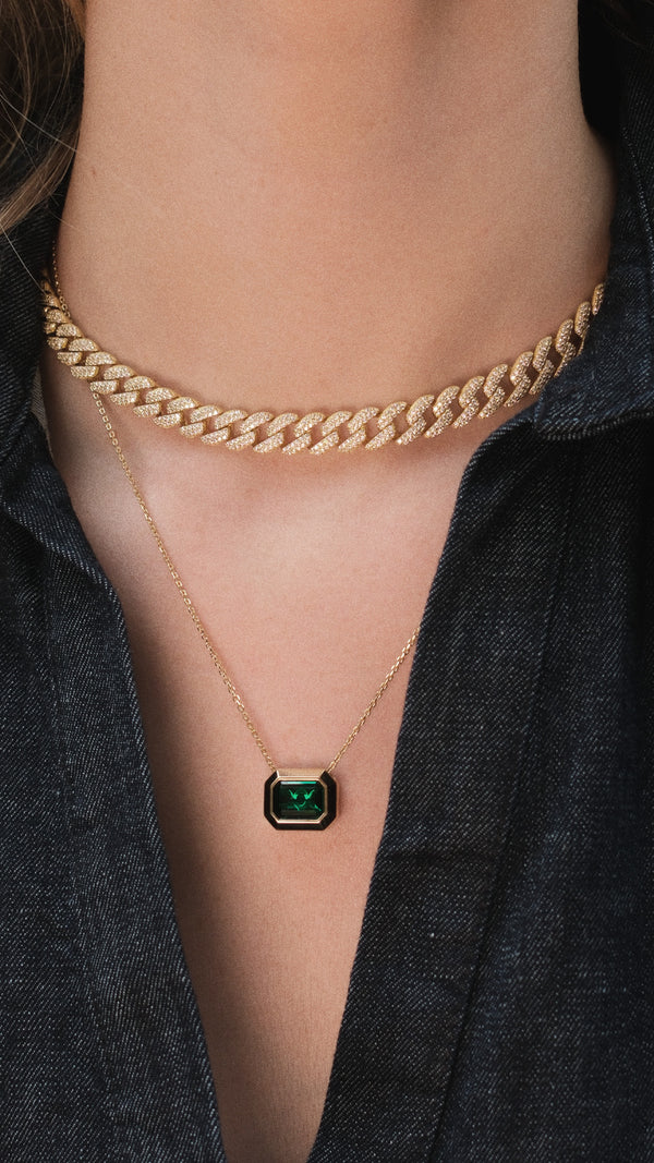Gold cuban chain necklace with a green gemstone pendant on a person wearing a dark denim dress.