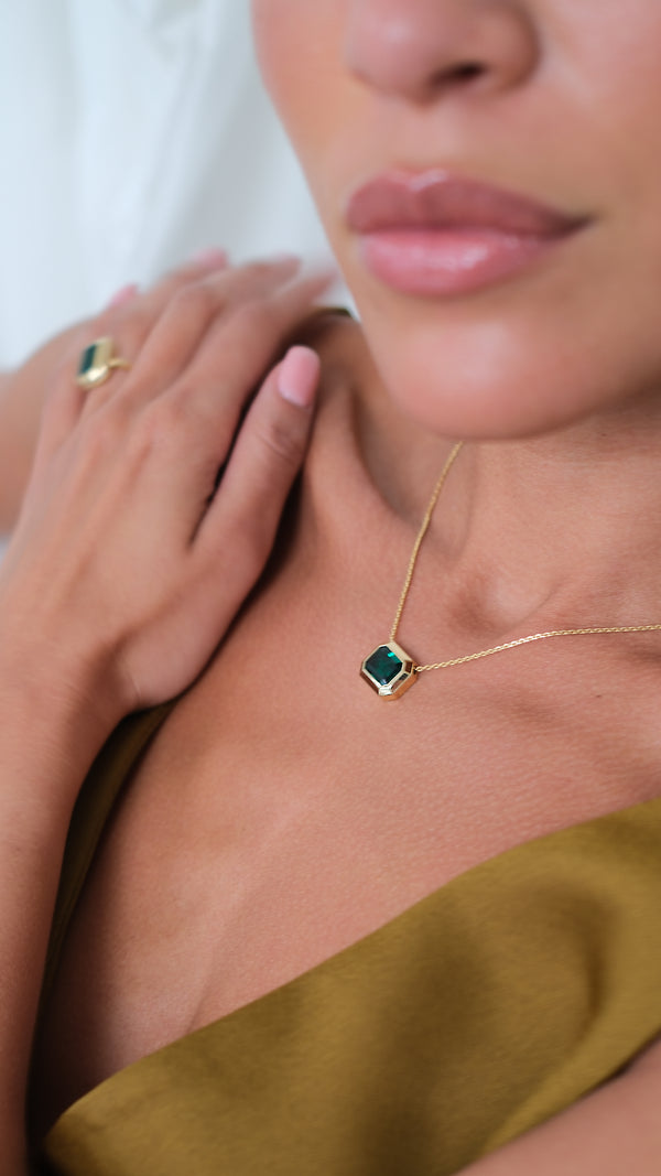 Woman wearing a gold necklace with a green gemstone pendant in a bezel setting.