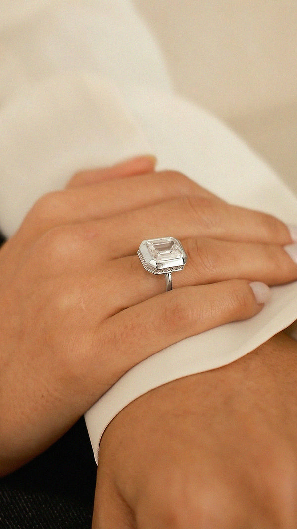Close-up side view of a hand wearing a silver emerald-cut cocktail ring. 