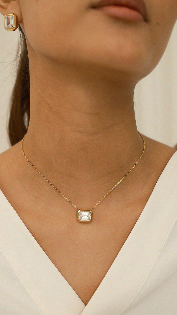 Necklace with an emerald-cut gemstone pendant worn by a person against a neutral background