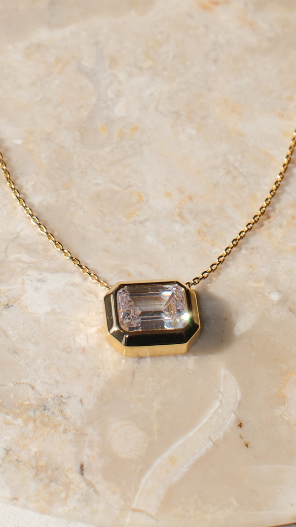 A close-up view of the gold Lily pendant necklace, showcasing the crisp, step-cut facets of the clear emerald-cut gemstone and the smooth, polished, heavy-duty gold bezel.