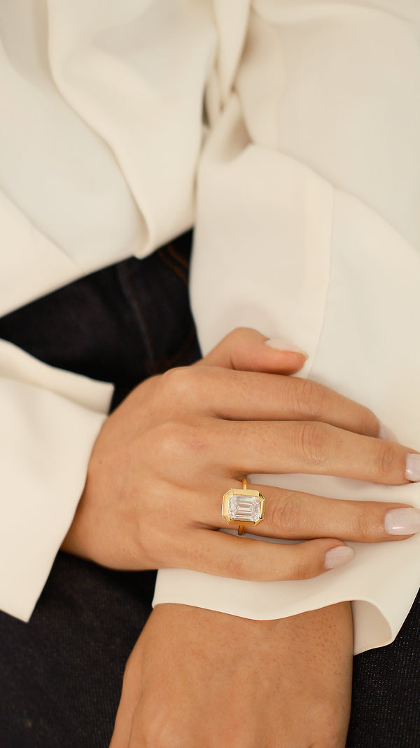 A model wearing the gold Lily emerald-cut ring on her ring finger, styled with a white shirt and dark denim. 