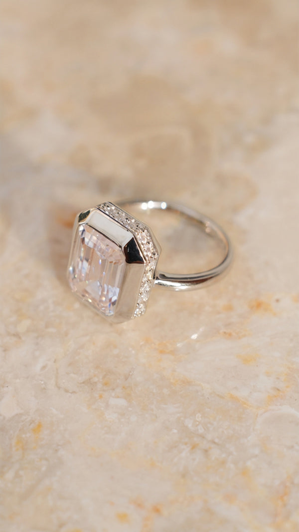 Side-profile view of a sterling silver Lily ring on a marble surface, highlighting the large emerald-cut gemstone in a chunky bezel setting with a hidden pavé halo of small stones underneath.