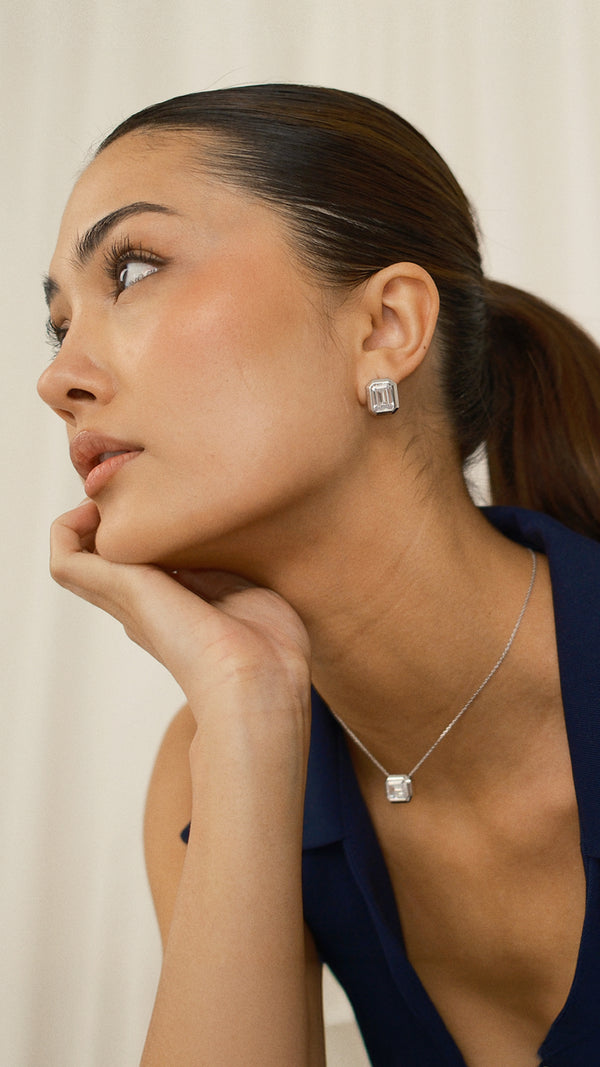 Woman wearing a silver emerald-cut earring and necklace against a neutral background