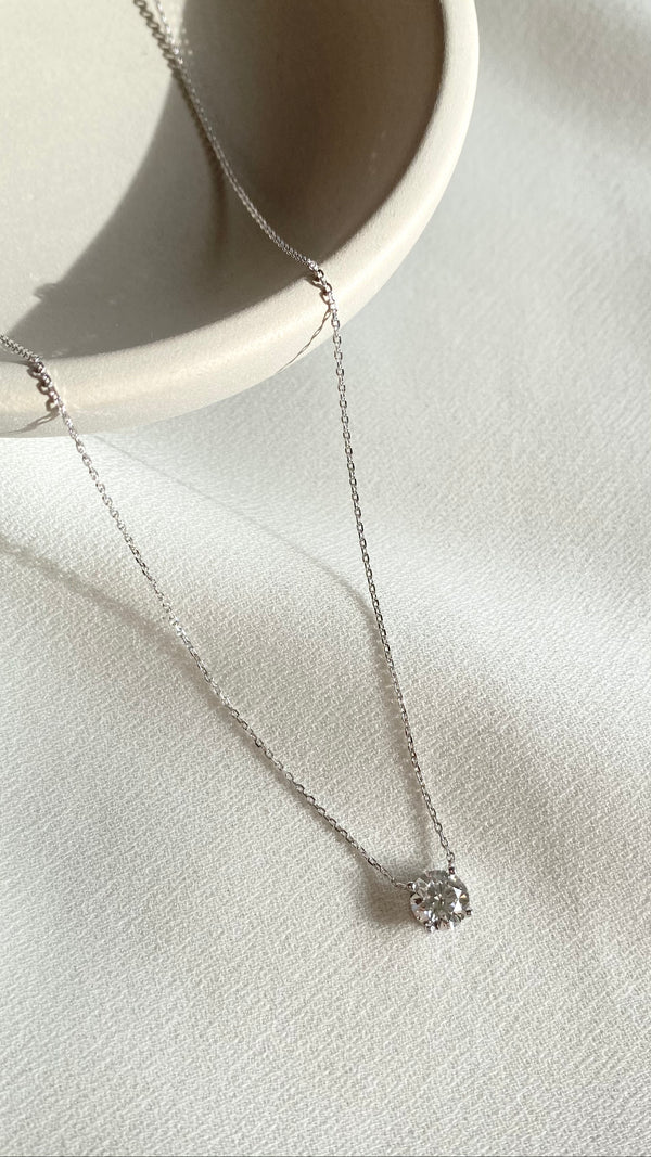 A solitaire diamond necklace set in 18K white gold, displayed on a white surface.
