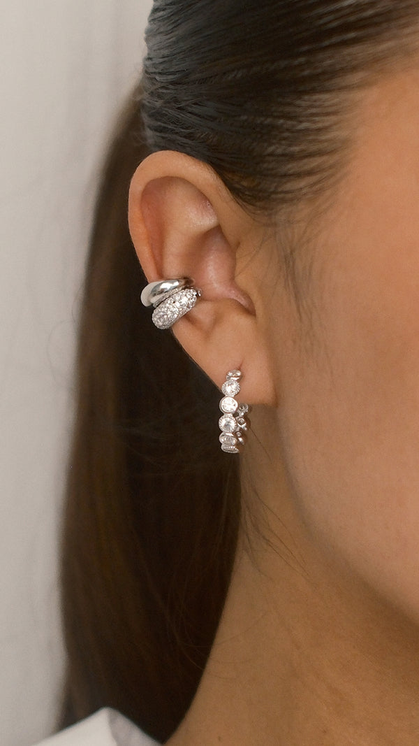 Close-up of an ear wearing a silver hoop earring with round gemtsones with stacked textured ear cuffs.