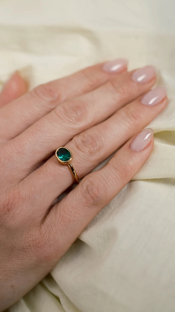 Close up of an oval bezel set emerald green cocktail ring