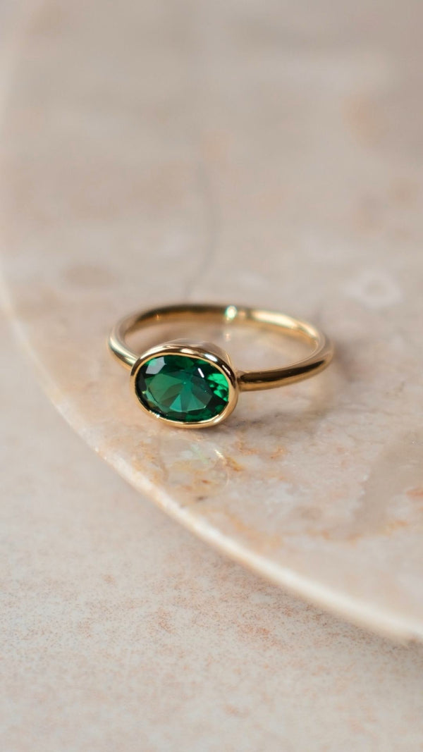 Oval cut emerald ring in a yellow gold bezel setting on a polished band