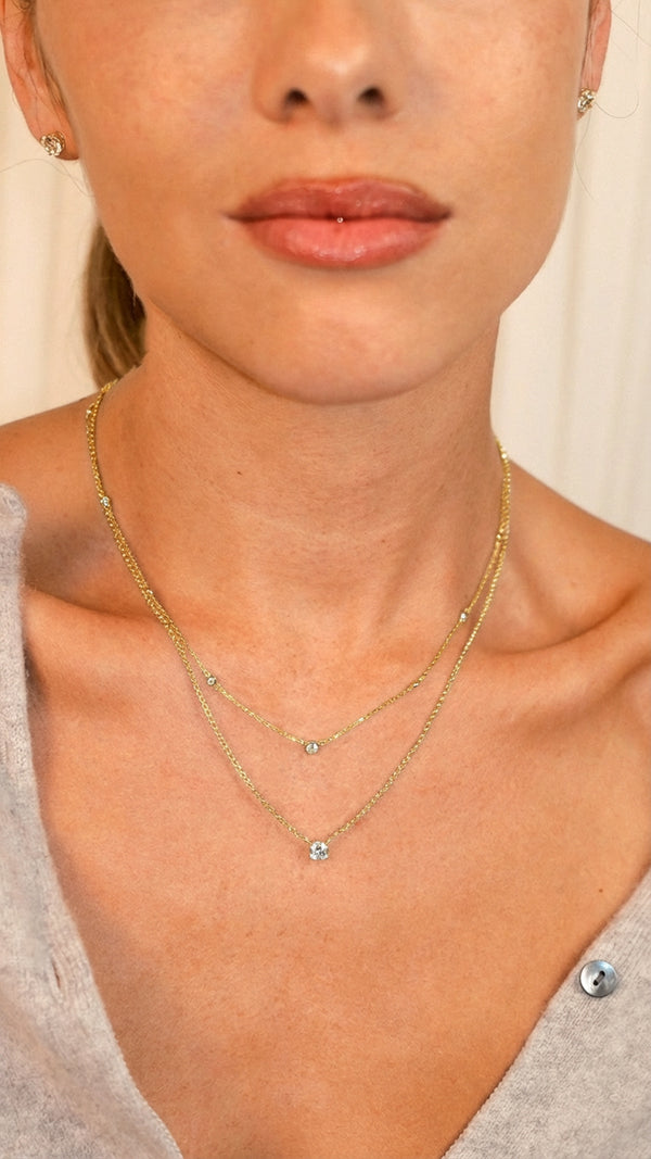 Layered gold station necklace and solitaire set worn at different heights.