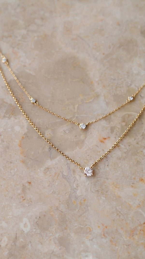 Detailed shot of a gold vermeil layered necklace with a solitaire pendant bottom layer and station style chain top layer.