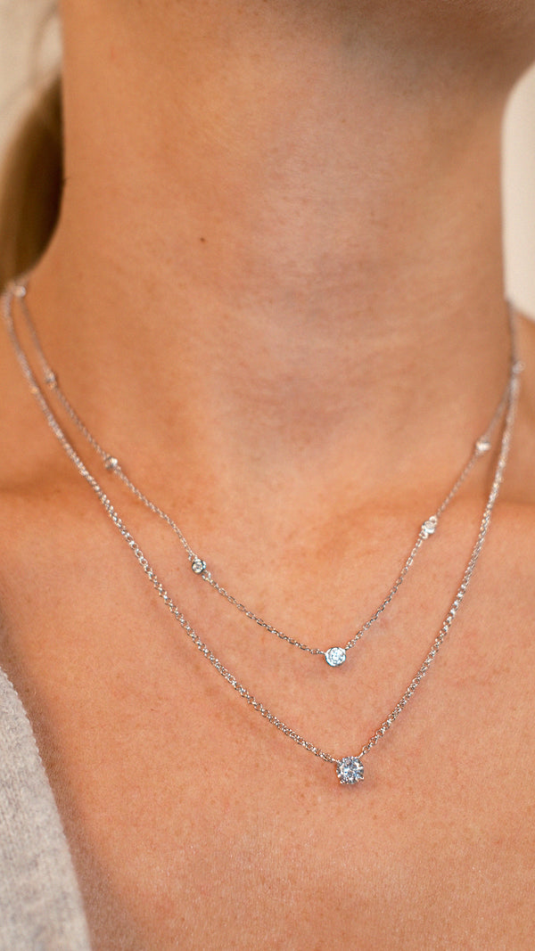 Close-up of a person wearing a pre layered silver necklace set with a round solitaire.