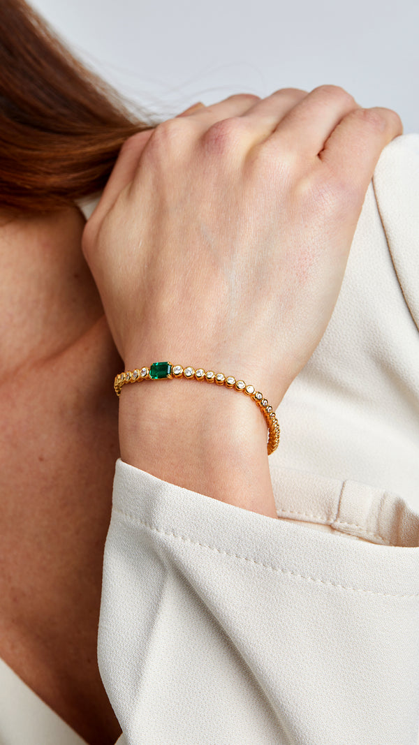 Brilliant-cut gemstone tennis bracelet with emerald accent.