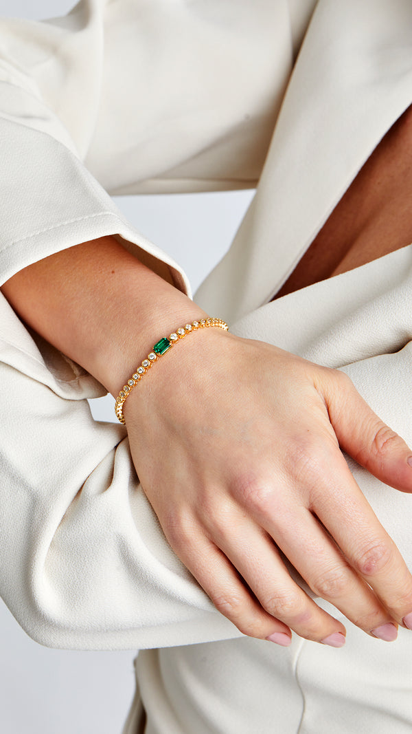 Adjustable gold bracelet with round and rectangular emerald-green stones.