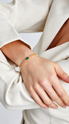 Adjustable gold bracelet with round and rectangular emerald-green stones.