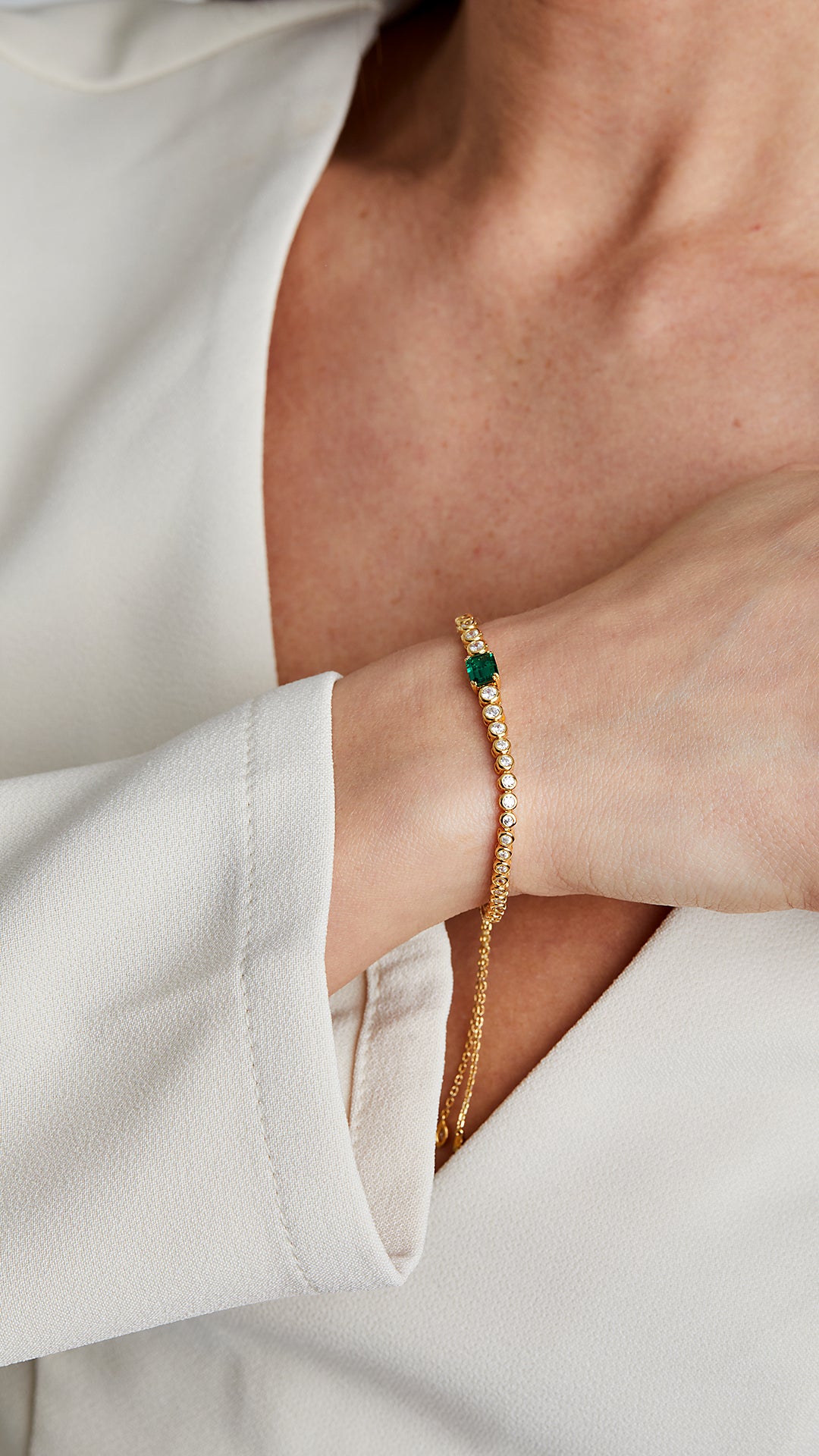Bezel-set stone bracelet with adjustable slider. Gold with round and emerald-green gemstones.