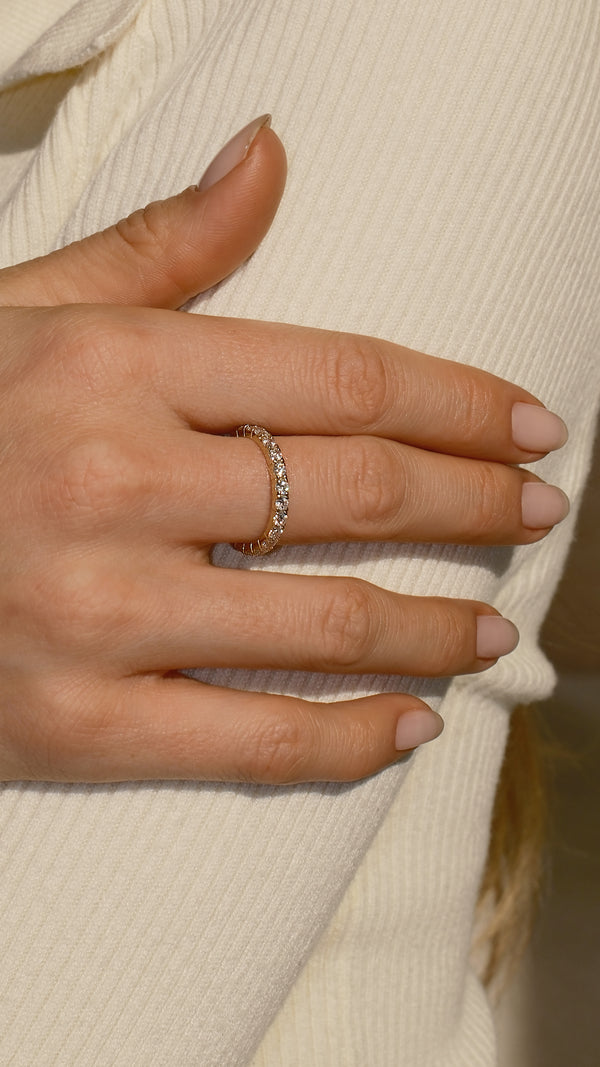A hand touching a jumper sleeve wearing a delicate 9k yellow gold eternity brand.