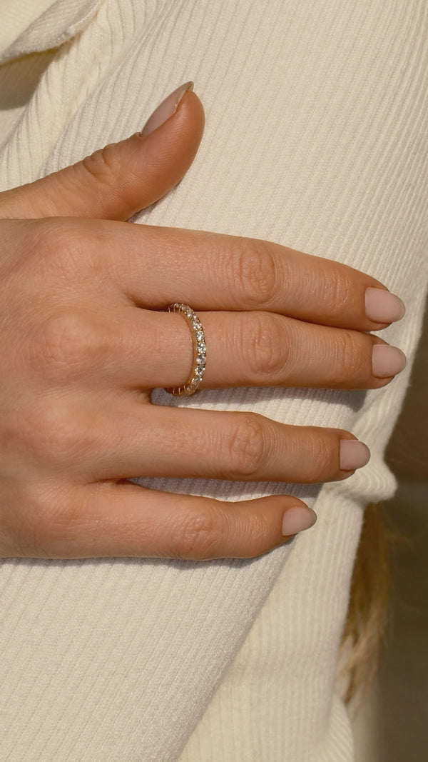 A hand touching a jumper sleeve wearing a delicate 9k yellow gold eternity brand.