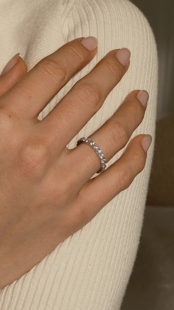 Close-up of a hand wearing a 9k solid gold eternity band with a blurred background