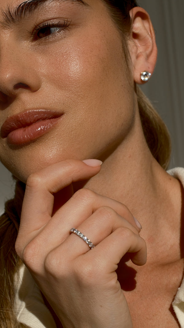 Close-up of a woman wearing an eternity ring and earring, with a neutral background