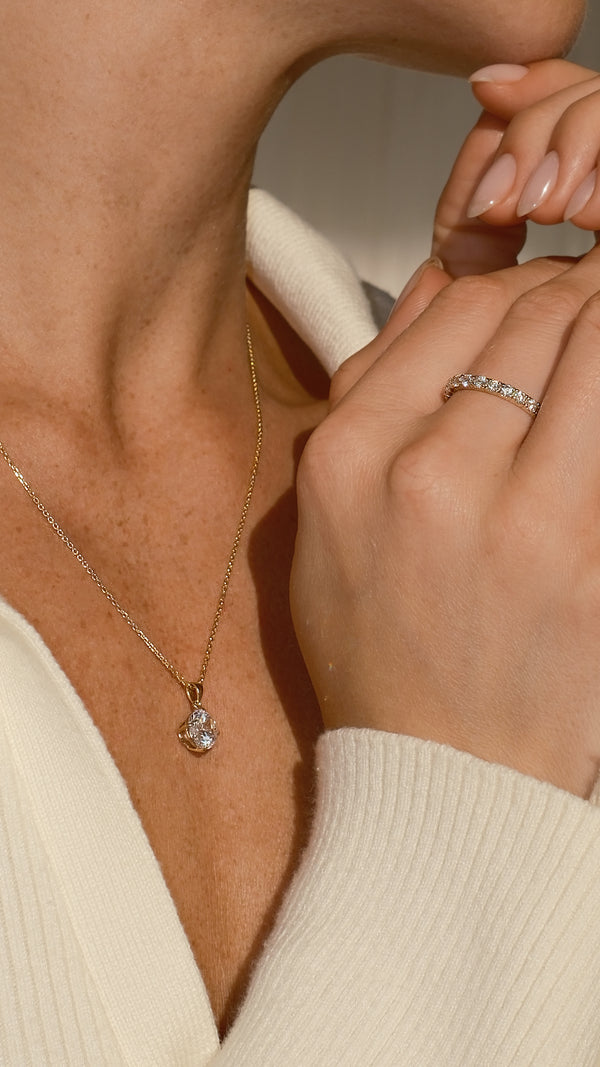 Close-up of a person wearing a gold necklace and  promise ring, with a neutral background.