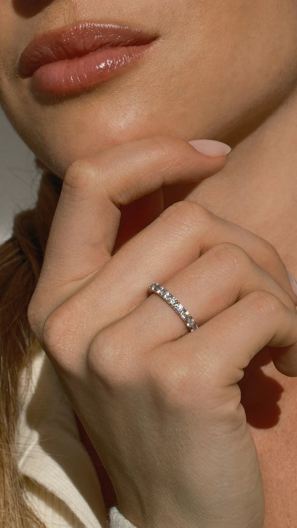 Close-up of a hand with a diamond style eternity ring, touching the chin.