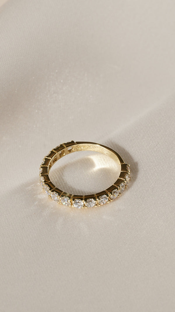 Top down still life view of a 9k solid yellow gold eternity ring with a row of polished round stones.