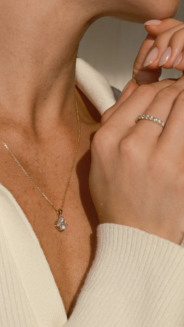 Close-up of a person wearing a gold necklace with a pendant paired with a solid gold eternity ring.