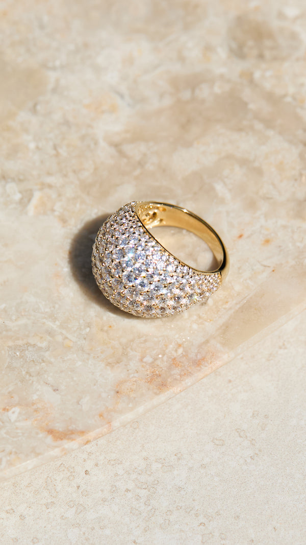 Gold dome ring with gemstone accents on a beige stone surface