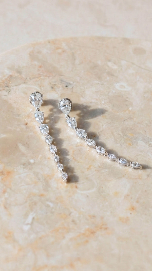 Silver earrings with pear shape drop stones on a beige stone surface