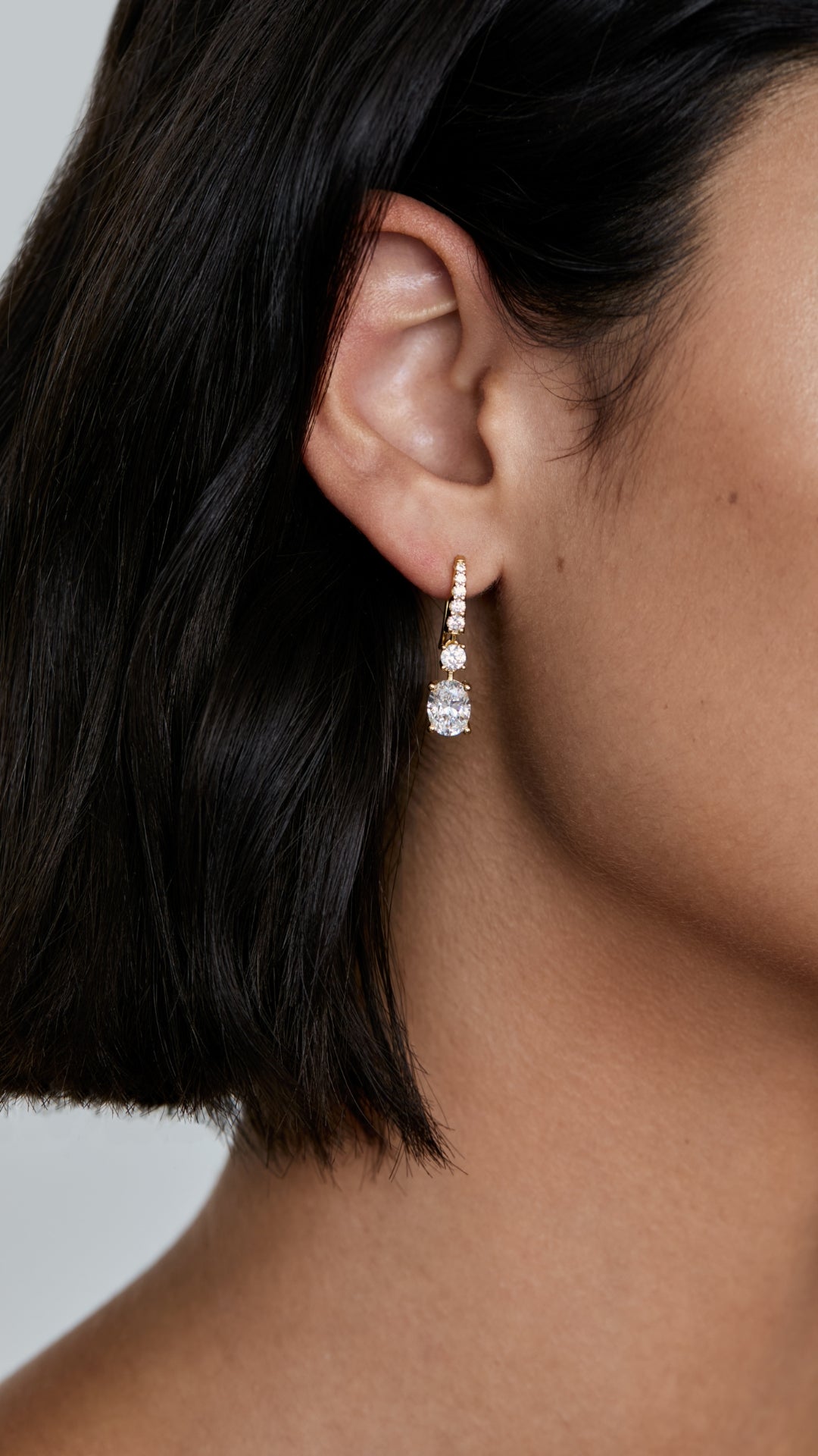 Close-up of an ear wearing an oval drop earring in gold vermeil with a blurred background