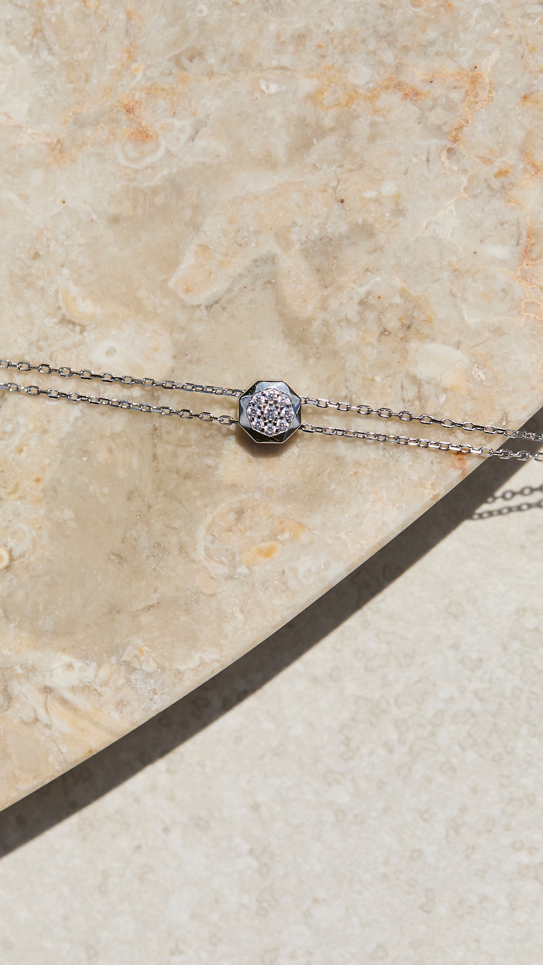 Silver necklace with a decorative adjustable slider on a beige stone surface