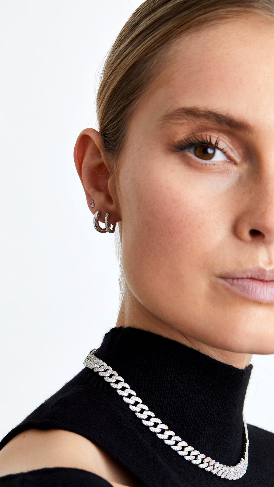 A close-up image of a woman wearing a large pavé sterling silver necklace with intricate pavé details and bold, chunky Cuban links.