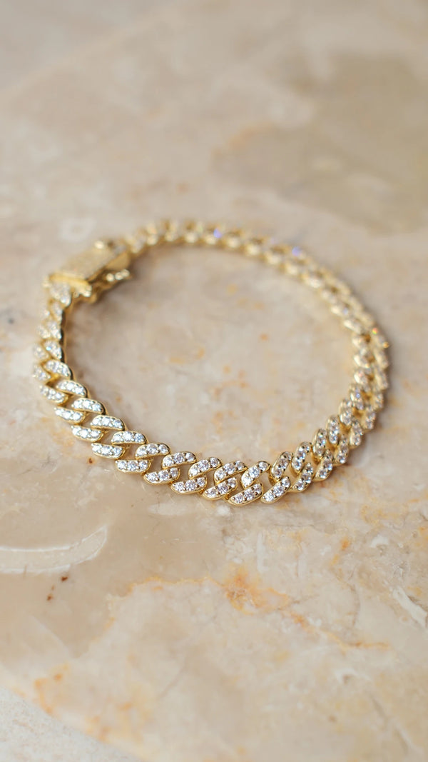 Gold link bracelet with gemstone detailing on a marble background. 