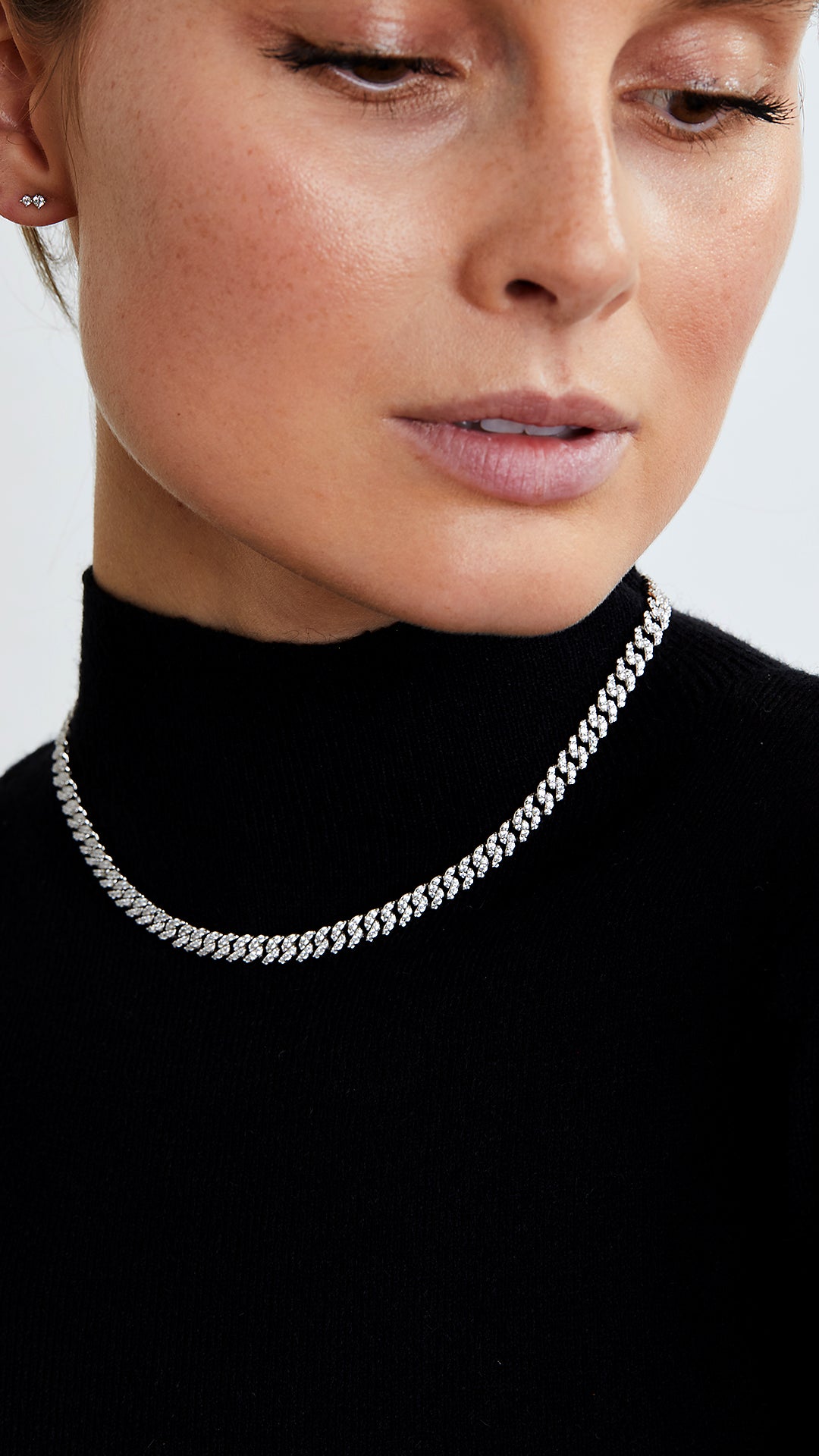 A person wearing a black turtleneck sweater and a small pave necklace with intricate pavé settings in silver.