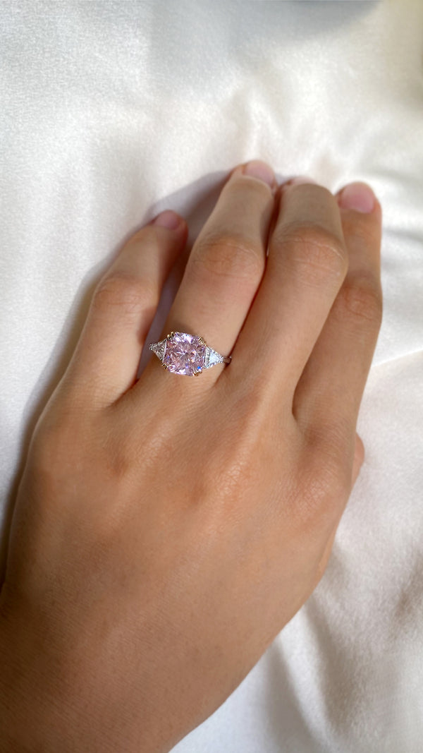 Top-down view of a classic trilogy ring featuring a vibrant, 3ct equivalent fancy pink modified round brilliant centre stone.